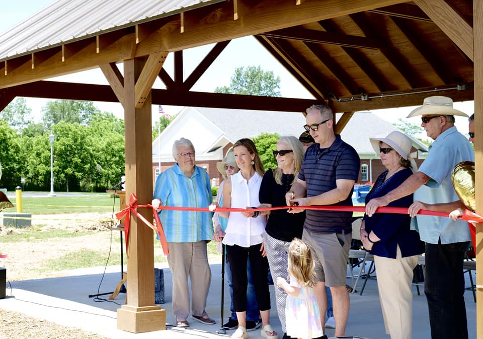 Ostrander mayor cuts the ribbon with large, gold scissors