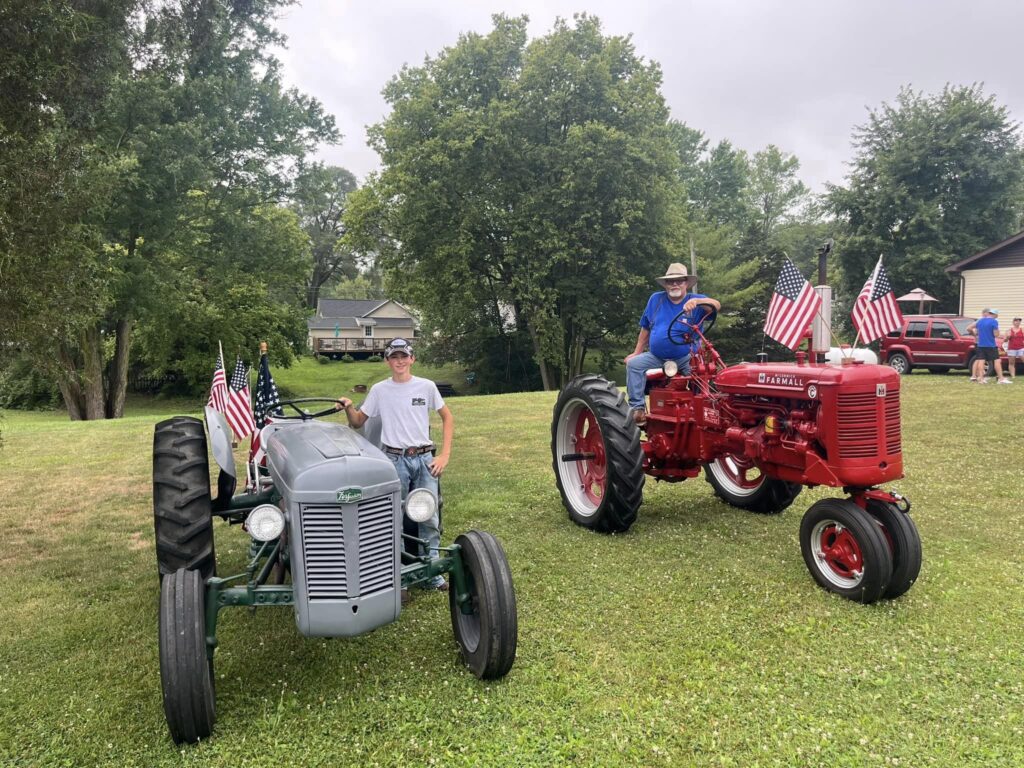 Two more old-fashioned tractors, a red Farmall and a gray Ferguson, both decorated with American flags